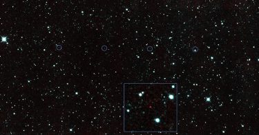 A rugged asteroid drifts against a dense field of bright stars in deep space.